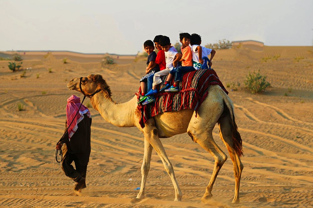 Tourists trying camel riding in Dubai desert